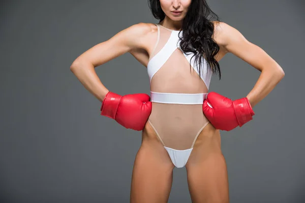 Cropped image of sexy sportive woman in white leotard and boxing gloves standing with hands akimbo isolated on grey — Stock Photo