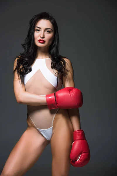 Seductive athletic woman in white swimwear and boxing gloves looking at camera isolated on grey — Stock Photo