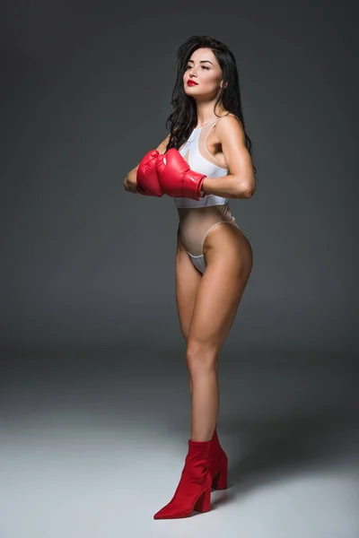 Mulher esportiva sexy em roupa de banho branca e luvas de boxe olhando para longe, em cinza — Fotografia de Stock
