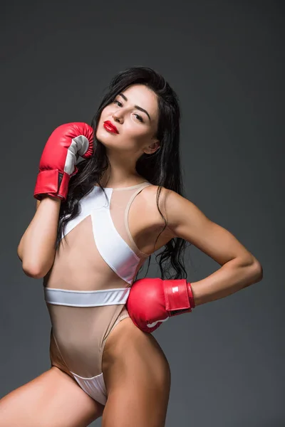 Mujer deportiva apasionada posando en traje de baño blanco y guantes de boxeo aislados en gris - foto de stock