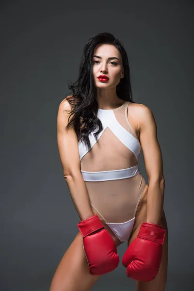 Сексуальная красивая спортивная женщина в белой спортивной одежде и боксерских перчатках, смотрящая на камеру, изолированную на сером — стоковое фото