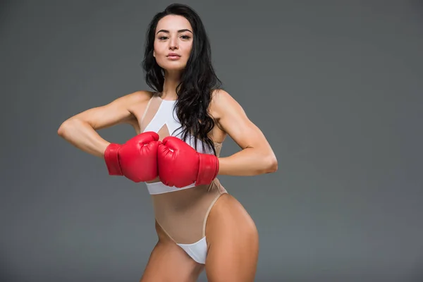 Сексуальная спортивная женщина в белом трико, показывающая руки в боксёрских перчатках, изолированных на сером — стоковое фото