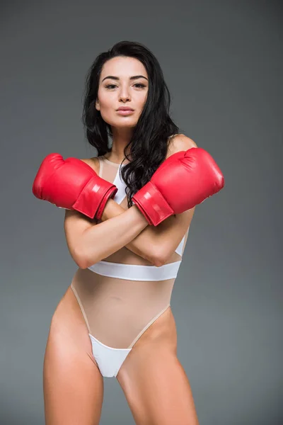 Attraktive sportliche Frau in weißer Badebekleidung mit verschränkten Armen in Boxhandschuhen vereinzelt auf grau — Stockfoto