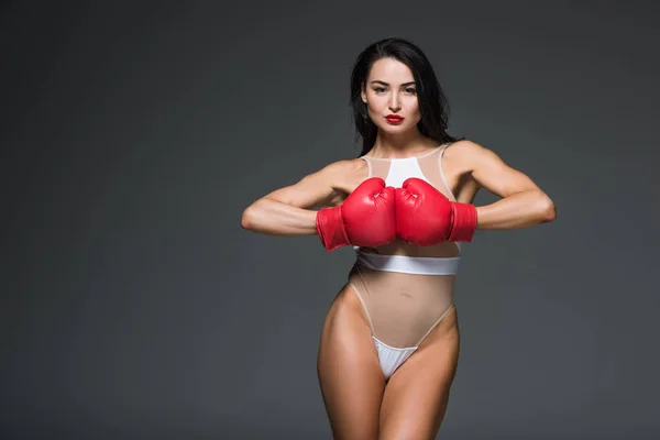 Сексуальная спортивная женщина в белых купальниках и боксерских перчатках, смотрящая на камеру, изолированную на сером — стоковое фото