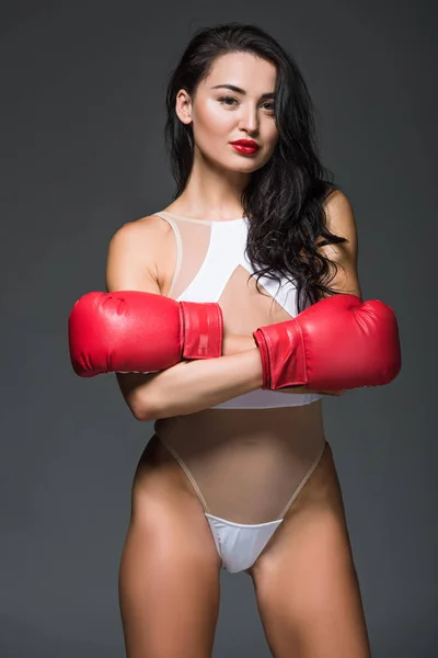 Sexy mujer deportiva en ropa deportiva blanca y guantes de boxeo de pie con brazos cruzados aislados en gris - foto de stock