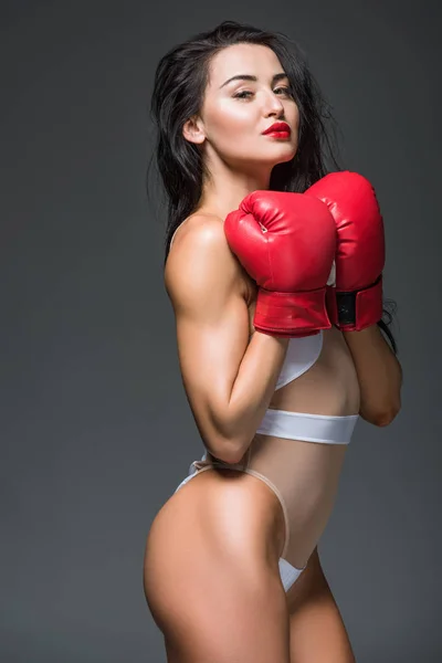 Vista lateral de mujer deportiva sexy en traje de baño blanco y guantes de boxeo aislados en gris - foto de stock