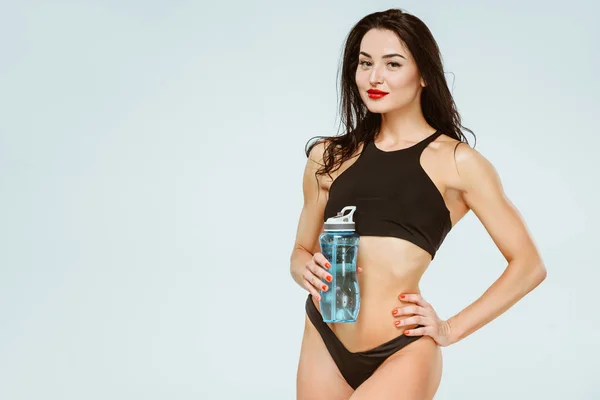 Schöne sexy Frau in Sport-BH und Höschen hält Sportflasche isoliert auf grau — Stockfoto