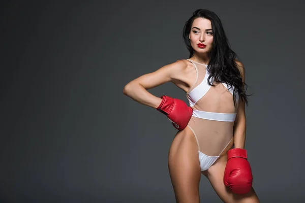 Спокуслива спортивна жінка в білому купальнику і боксерські рукавички позує ізольовано на сірому — стокове фото