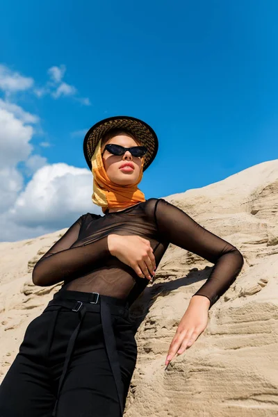 Attrayant femme à la mode posant près de dune de sable avec ciel sur fond — Photo de stock