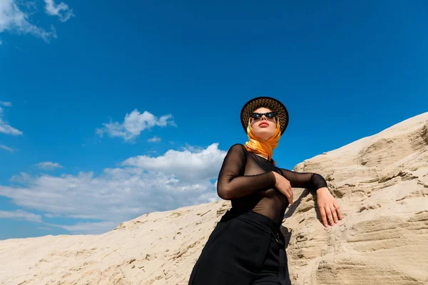 Vista inferior da mulher elegante posando perto de duna de areia com céu azul no fundo — Fotografia de Stock