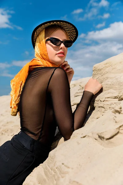 Beautiful young woman posing in stylish hat near sand dune — Stock Photo
