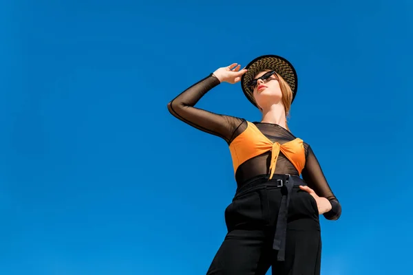 Chica elegante posando en gafas de sol de moda y sombrero, cielo azul en el fondo - foto de stock
