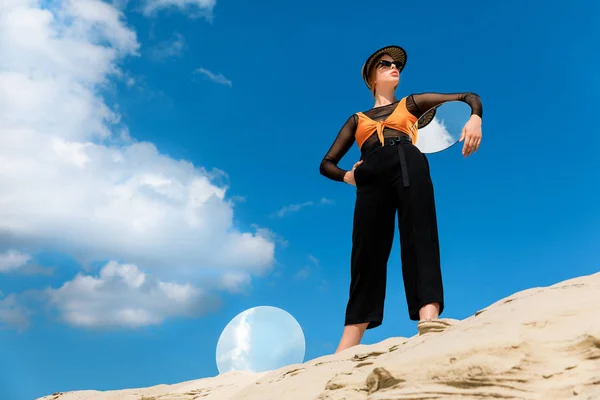 Elegante bella modella in abiti eleganti in posa con specchi rotondi con riflesso del cielo nuvoloso — Foto stock