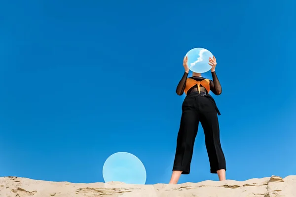 Mulher elegante segurando espelho com reflexo do céu azul na frente do rosto — Fotografia de Stock