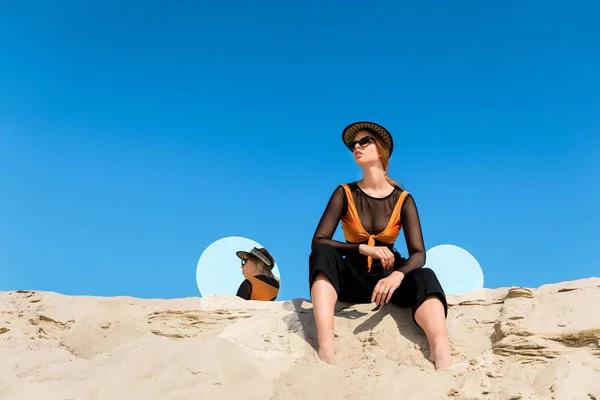 Modelo de moda posando sobre arena con espejos redondos con reflejo del cielo azul - foto de stock