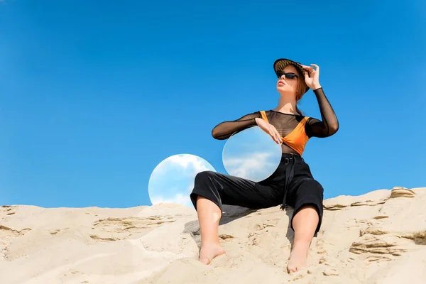 Modèle élégant posant sur une dune avec des miroirs ronds avec réflexion du ciel bleu — Photo de stock