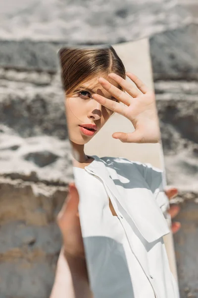 Attraente donna tenendo pezzo di specchio e guardando il suo riflesso — Foto stock