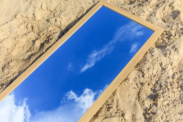 Mirror with reflection of blue cloudy sky lying on sand — Stock Photo
