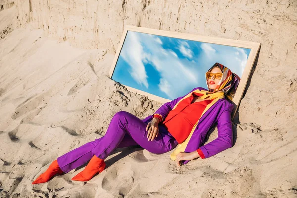 Beautiful model in fashionable clothes lying on mirror with reflection on cloudy sky — Stock Photo