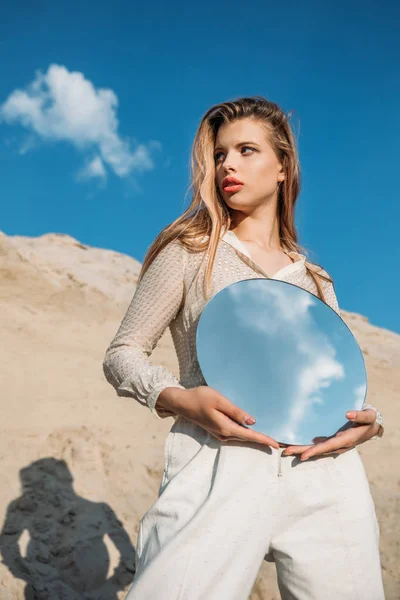 Attractive stylish girl holding round mirror with reflection of cloudy sky — Stock Photo