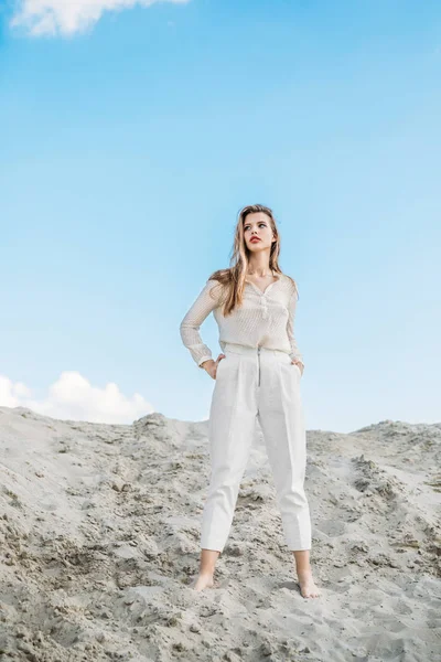 Atractiva mujer de moda en ropa blanca posando en la duna de arena - foto de stock