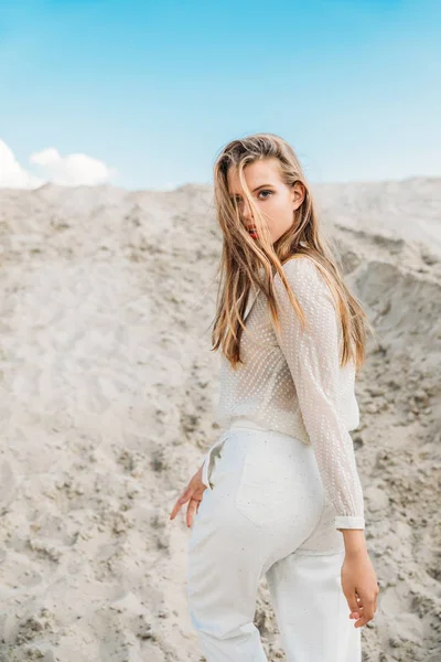 Hermosa chica rubia en ropa blanca posando en el desierto de arena - foto de stock