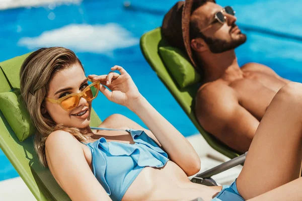 Young couple in sunglasses relaxing on sunbeds at poolside — Stock Photo