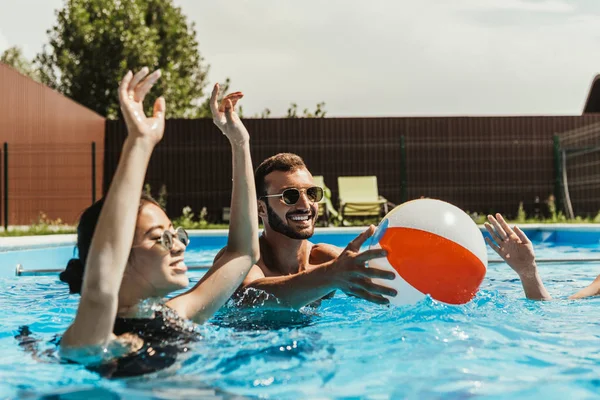 Multiethnic friends playing with beach ball in swimming pool — Stock Photo
