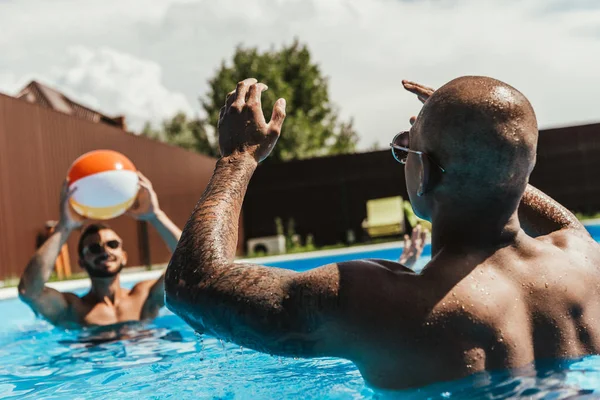 Multicultural men playing with beach ball in swimming pool — Stock Photo