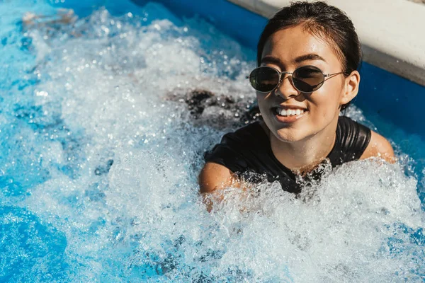 Smiling asian girl in sunglasses swimming in pool — Stock Photo