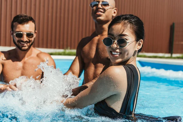 Amigos multiculturais brincando na água na piscina — Fotografia de Stock
