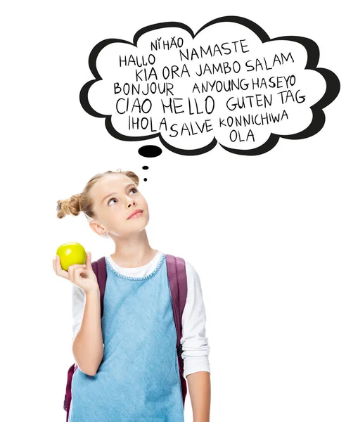 Niño de la escuela sosteniendo manzana y mirando hacia arriba con palabras en diferentes idiomas en la burbuja del habla, aislado en blanco - foto de stock