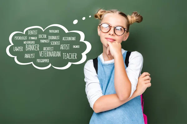 Pensive schoolchild in glasses looking up near blackboard with different professions in speech bubble — Stock Photo