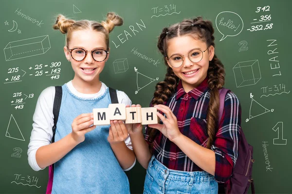 Écoliers tenant des cubes en bois avec des mots mathématiques près du tableau noir avec des symboles mathématiques — Photo de stock
