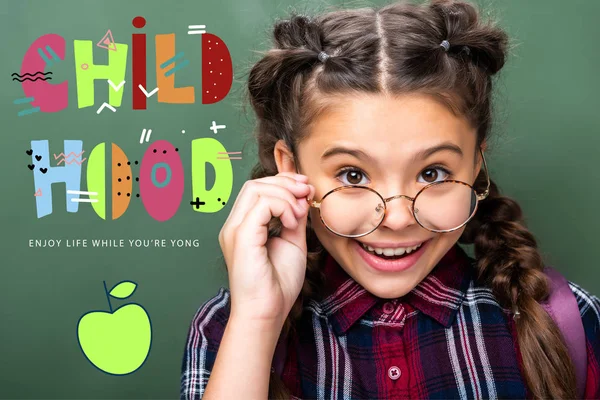 Portrait of schoolchild looking above glasses near blackboard, with 