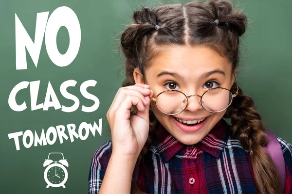 Portrait of schoolchild looking above glasses near blackboard, with 