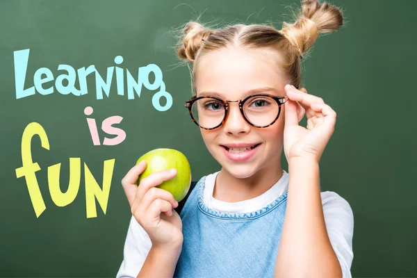 Schoolchild holding apple and touching glasses near blackboard, with 