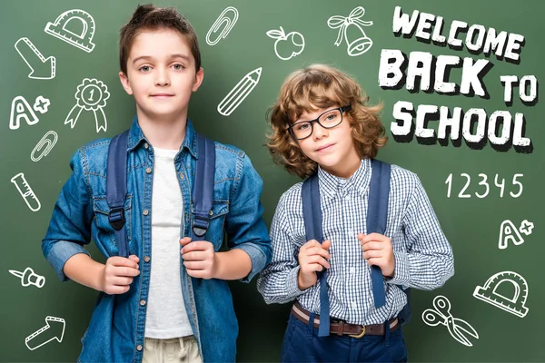 Schoolboys with backpacks looking at camera near blackboard, with icons and 