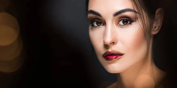 Schönes Modell mit Make-up posiert auf schwarz mit goldenem Bokeh — Stockfoto