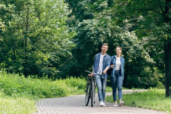 Счастливая молодая пара прогуливаясь по парку с винтажным велосипедом — стоковое фото