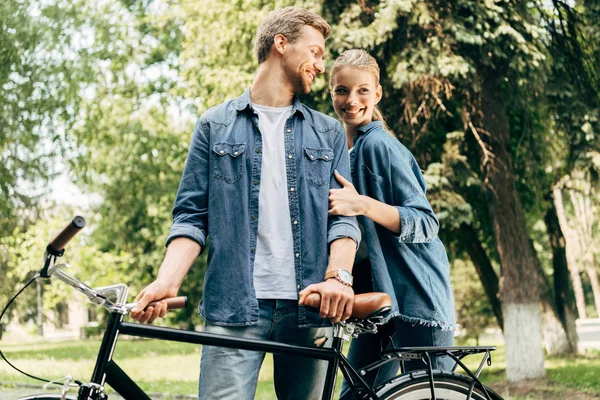 Beautiful young couple with vintage bicycle standing at park — Stock Photo