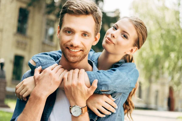 Beautiful young woman embracing her boyfriend from behind and looking at camera — Stock Photo