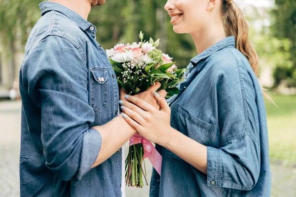 Cropped shot of young couple holding flower bouquet at park — Stock Photo