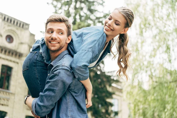 Happy young man carrying his girlfriend on shoulder at park — Stock Photo