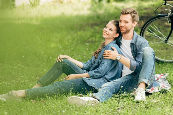 Hermosa pareja joven sentado en la hierba en el parque juntos - foto de stock