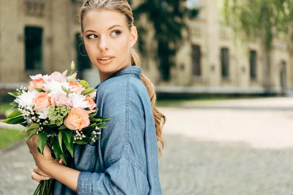 Attrayant jeune femme avec bouquet de fleurs regardant loin — Photo de stock