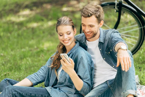 Glückliches junges Paar nutzt Smartphone gemeinsam im Park — Stockfoto