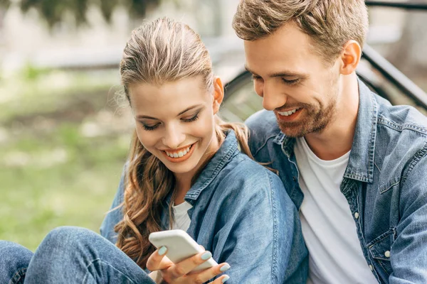 Beau jeune couple en utilisant smartphone ensemble au parc — Photo de stock