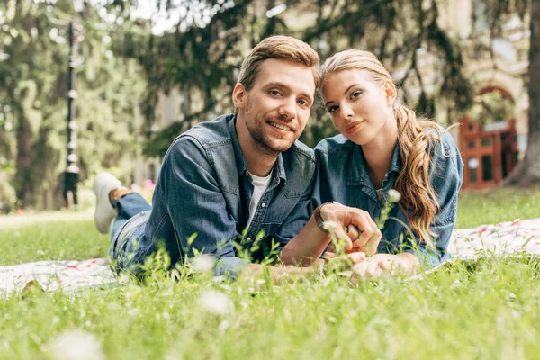 Feliz jovem casal deitado na grama no parque e olhando para a câmera — Fotografia de Stock