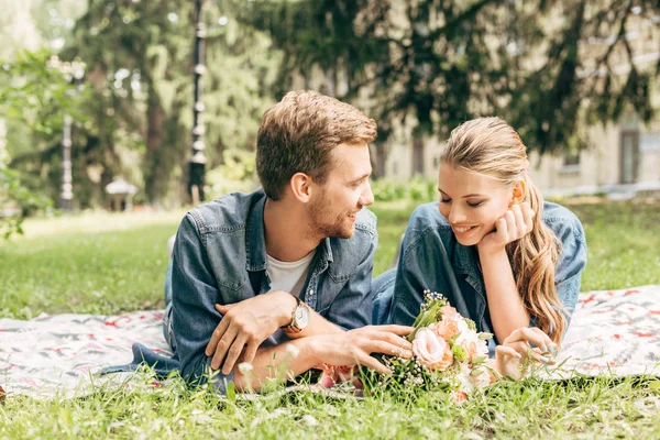 Feliz joven pareja acostada en la hierba en el parque y el coqueteo - foto de stock